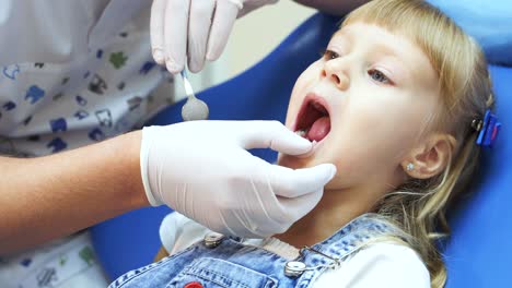 A little girl opens her mouth and shows the teeth to the dentist for treatment. Doctor's hands in medical gloves with a dental tool
