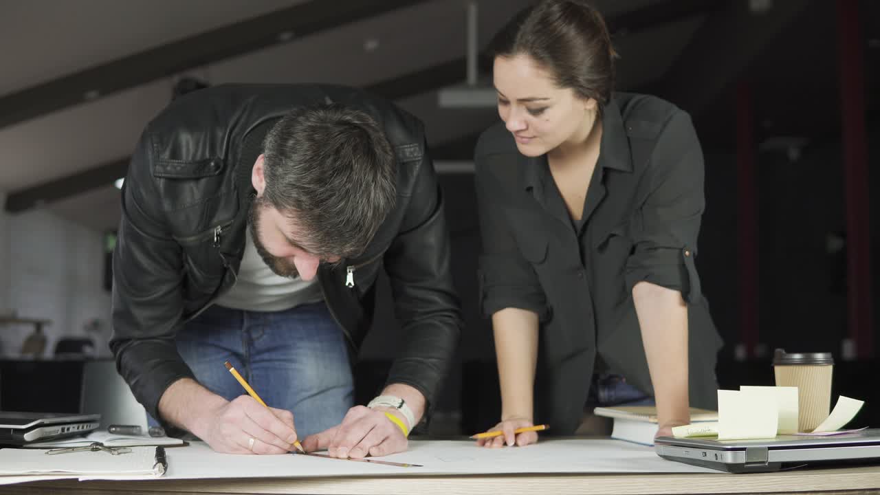 joven hombre y mujer trabajando en un proyecto, dibujando y pensando en una oficina moderna. usando brújula. taza de café y portátil en la mesa. filmado en 4k.