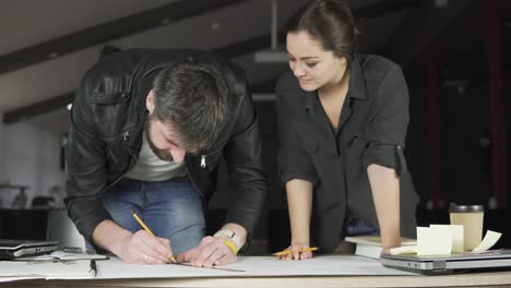 young man and woman working on a project, drawing and thinking in modern office. using compass. coffee cup and laptop on the table. shot in 4k.