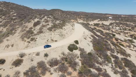 aerial: car driving on mountain dirt road through desert, 4k drone tracking view