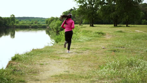 a girl in a pink jacket and black pants runs near the river in headphones preparing for the marathon