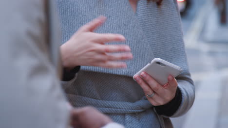 tilt shot of two millennial business colleagues holding smartphones and while talking to each other, close up, selective focus