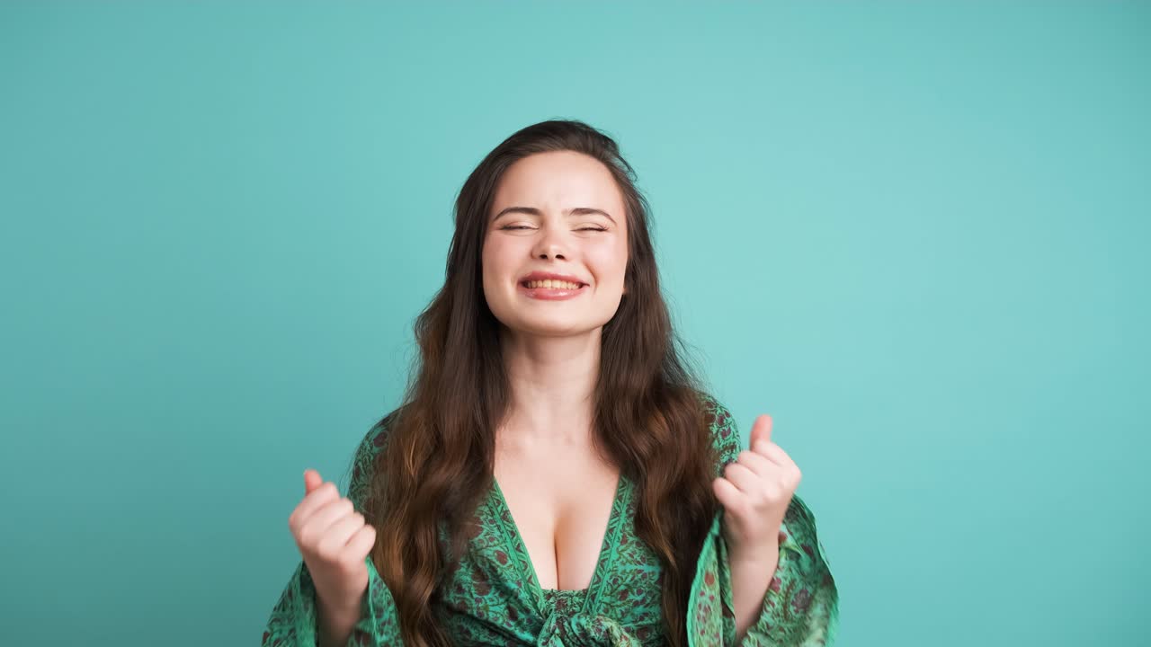 Successful young woman clenching fists in blue studio