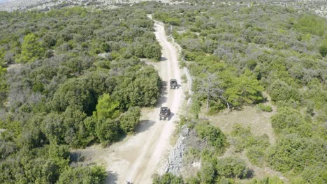 aerial follow shot of sandrail buggy cars riding on rough and unpaved terrain amidst green land