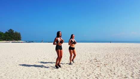 smiling beautiful girls with athlete bodies warming up on peaceful exotic beach with white sand at sunrise on a bright blue sea and sky background in bali
