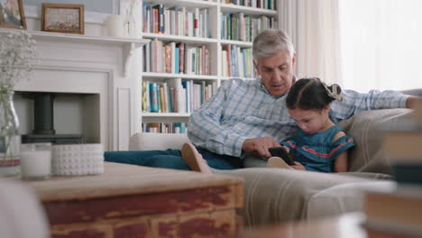 Abuelo-Feliz-Mostrando-A-La-Niña-Cómo-Usar-Un-Teléfono-Inteligente-Enseñando-A-Su-Nieta-Curiosa-Tecnología-Moderna-Niño-Inteligente-Aprendiendo-Teléfono-Móvil-Sentado-Con-El-Abuelo-En-El-Sofá