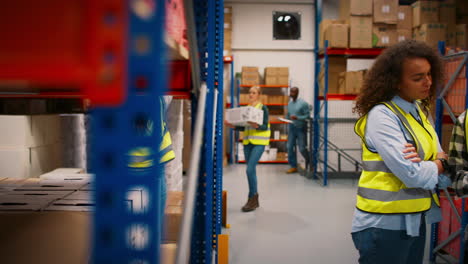 female team leader with digital tablet in busy warehouse training male intern standing by shelves