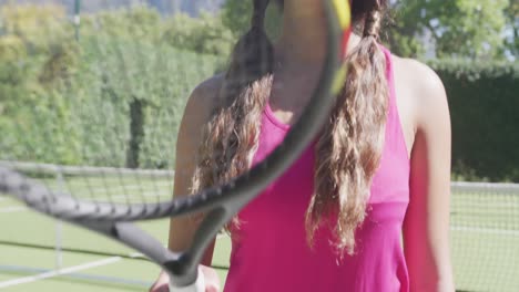 Portrait-of-happy-biracial-woman-with-tennis-racket-in-garden-on-sunny-day