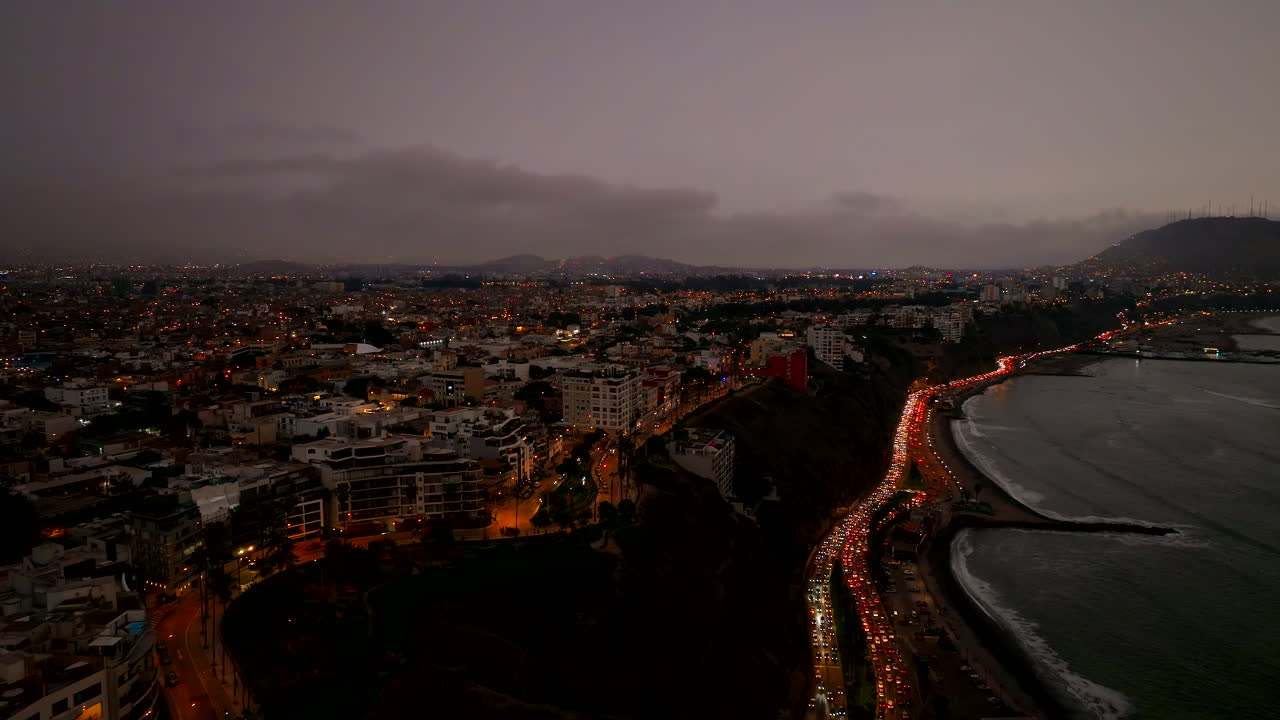 Dramatic drone establishing of Lima, Peru cityscape at sunset with deep red sky and buildings, cars illuminate road