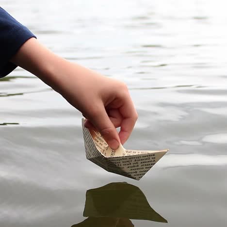 the boy playing near water. the boy playing launches a paper boat