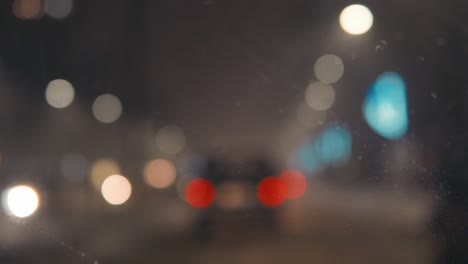 vista borrosa de la ciudad. fondo borroso con las luces de la ciudad por la noche. montar la máquina por carretera. nevadas en la ciudad. limpiadores de parabrisas de automóviles limpian la nieve de la ventana.