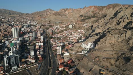 aerial drone shot over buildings and houses alongside two way main road at the foothills of a mountain in la paz, bolivia on a sunny day