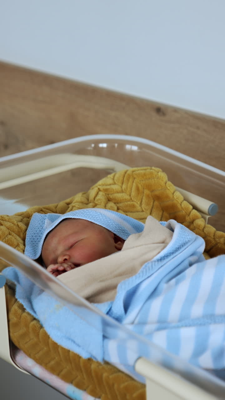 Hospital crib with a newborn sleeping in it. Lovely kid covered in blankets moves in his sleep. Vertical video