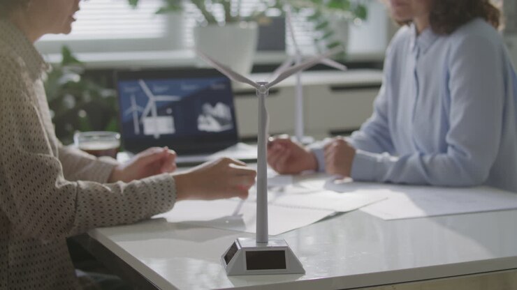 Wind Turbine Model on Office Desk, Two Female Engineers Talking in Background