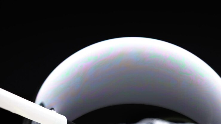 A soap bubble displays vibrant color reflections against a dark background, highlighting its delicate structure and fluid motion