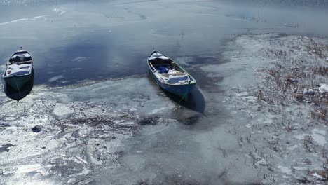 aerial shot of the lake, half-frozen, and the boats docked on the shore in winter time