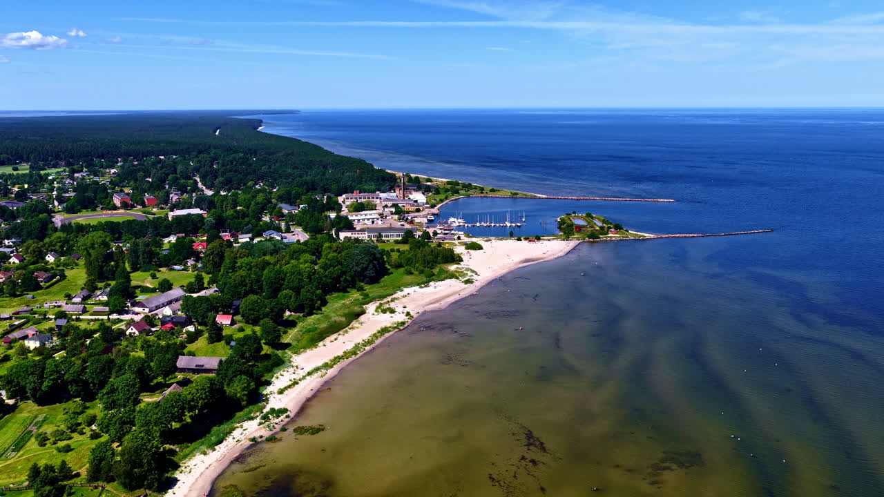 A spectacular high-angle drone shot reveals the picturesque village of Engure in Latvia, showcasing its charming marina, sandy beach, and lush forests stretching along the beautiful Baltic Sea coast