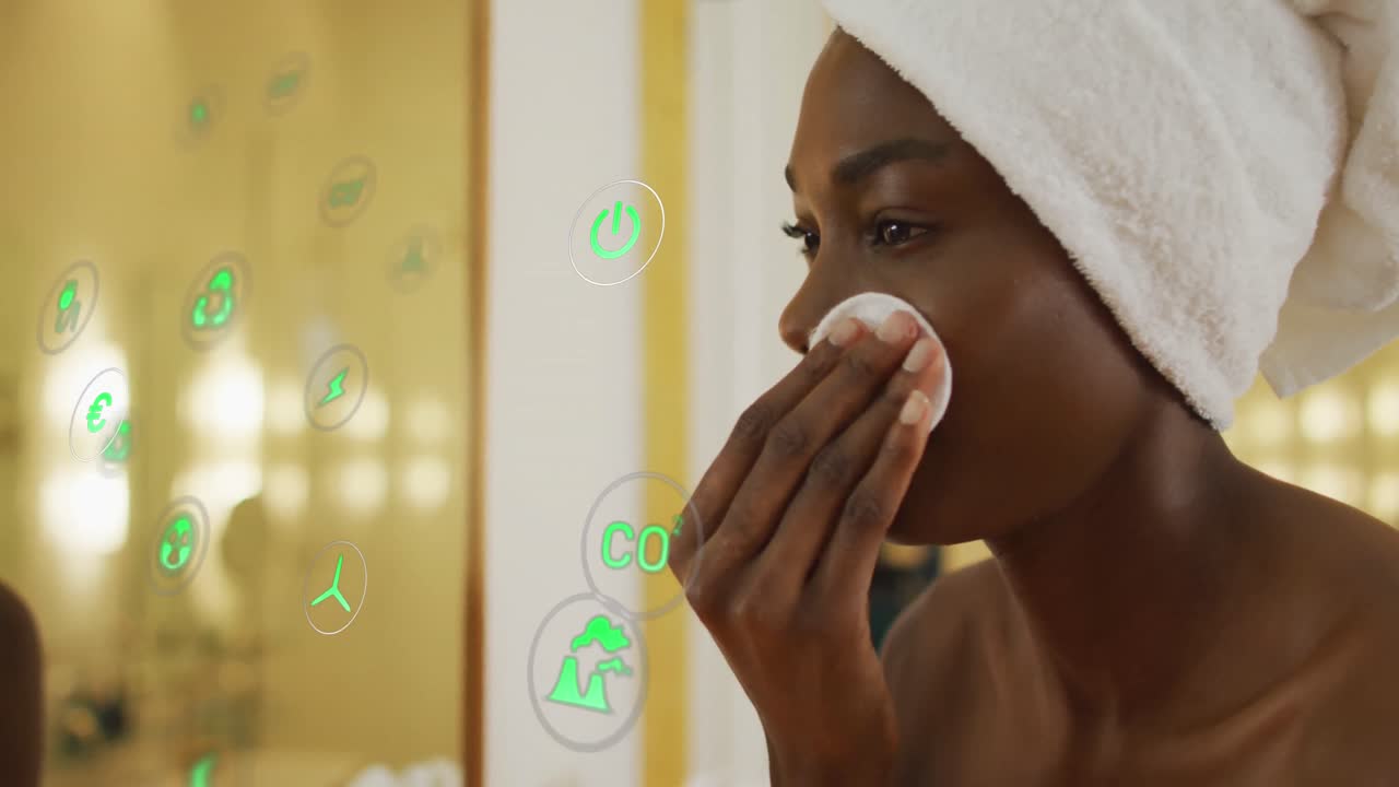 Animation of icons over african american woman cleansing face in bathroom