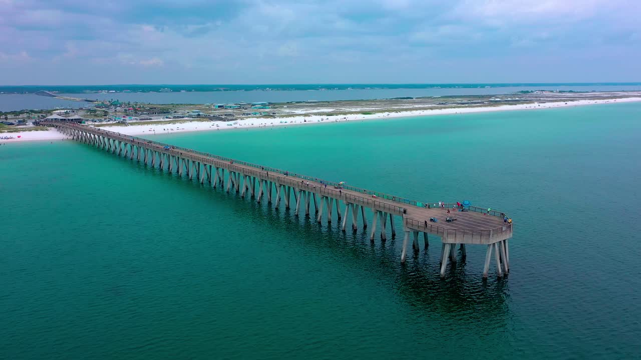 Vista aerea con drone in panoramica verso destra del molo di Navarre Beach, Florida, con alcune nuvole scure e la spiaggia di sabbia bianca sullo sfondo