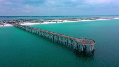 aerial drone panning right view of the navarre beach florida pier with some dark clouds and the white sand beach in the background