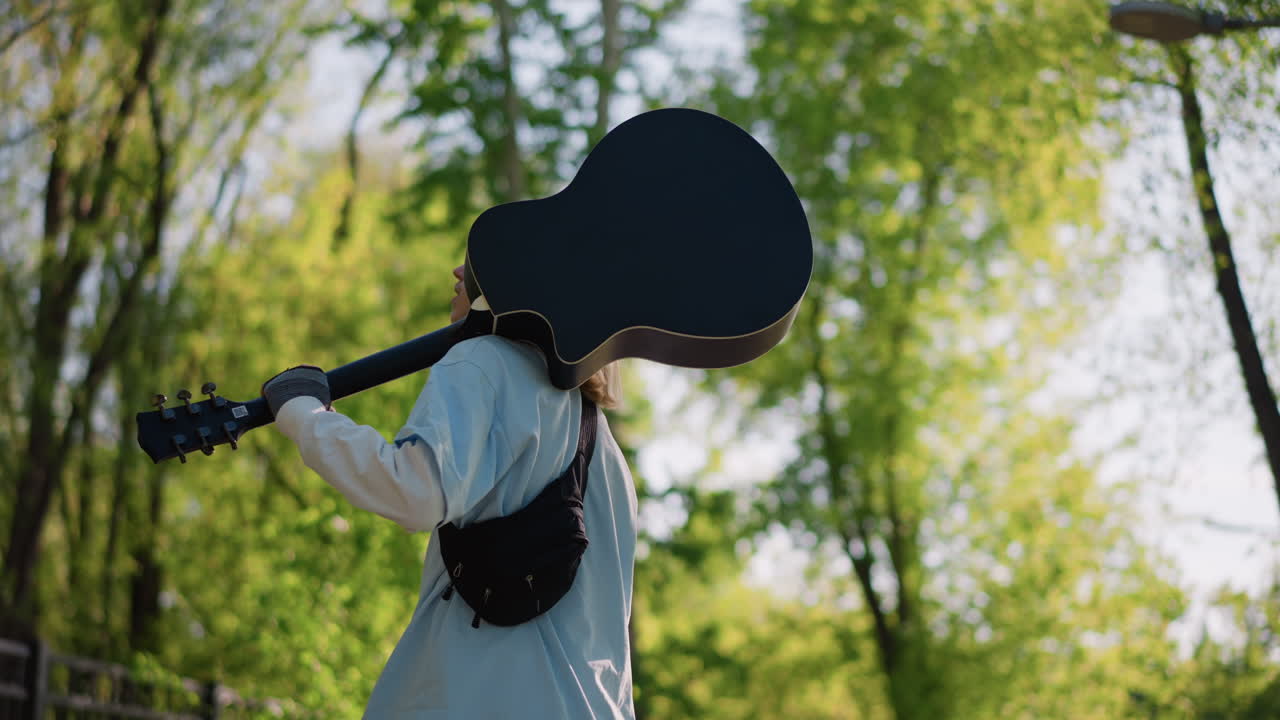 giovane chitarrista bianco che cammina in un parco illuminato dal sole, con la chitarra acustica a tracolla, lenti movimenti di macchina cinematografici che mostrano espressioni pensierose, momenti da cantautore e artista di strada, foglie sognanti retroilluminate, indie folk