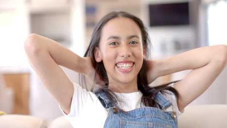 smiling teenage girl in denim overalls relaxing with hands behind head