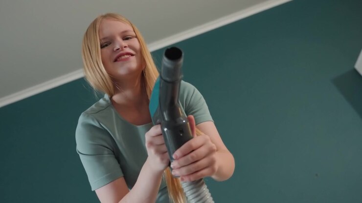 Donna bianca che aspira giocosamente la casa, proprietaria di casa sorridente che balla con il tubo, bocchetta senza fili che luccica, interno caldo color verde acqua, inquadrature gioiose dal basso, atmosfera di lifestyle, le inquadrature ritraggono la proprietaria di casa, intrattenitrice.