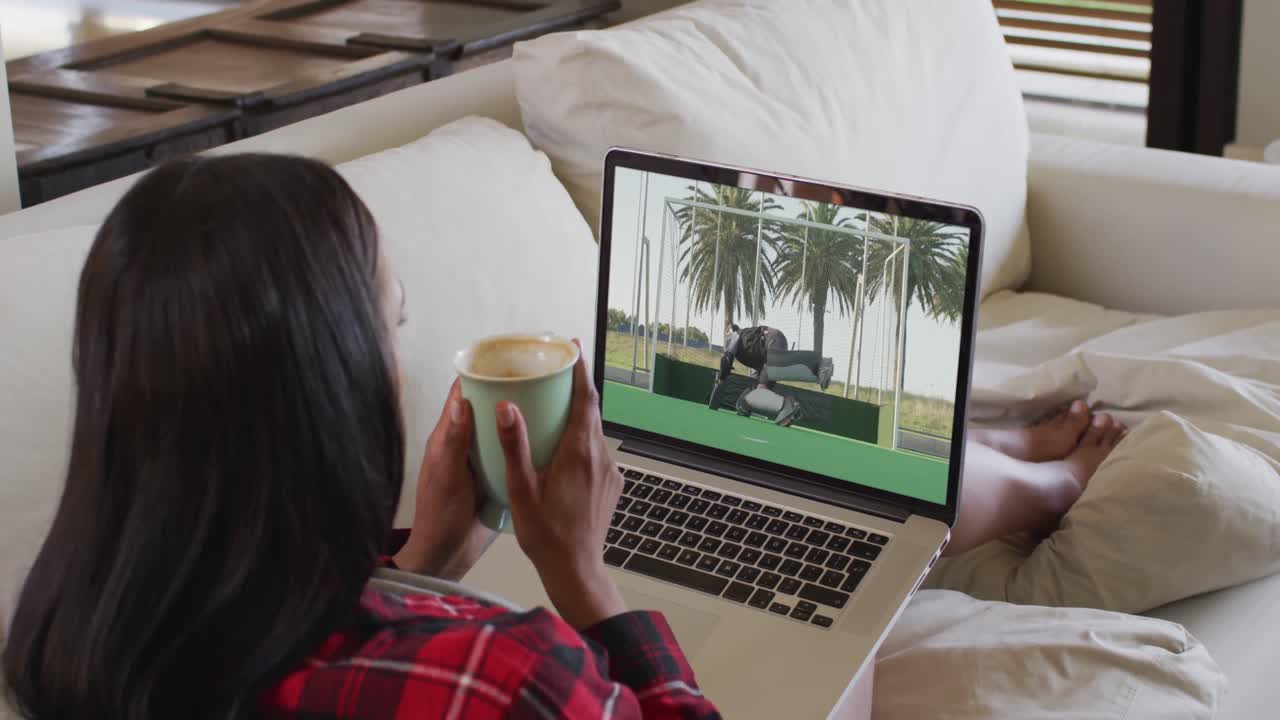 compuesto de una mujer sentada en casa sosteniendo un café viendo un partido de hockey en una computadora portátil