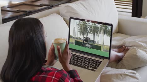 compuesto de una mujer sentada en casa sosteniendo un café viendo un partido de hockey en una computadora portátil