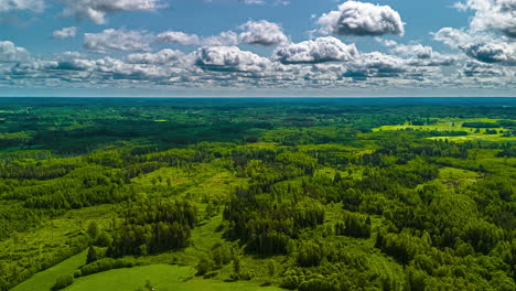 Clouds casting shadows over hills, fields, and dense forest terrain, aerial hyperlapse on bright day