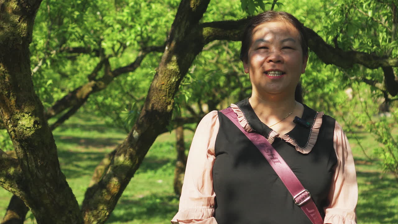 A young Asian woman is speaking near a plum tree in an orchard.