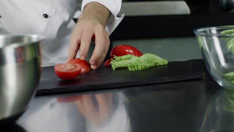 Chef-cooking-fresh-salad-at-kitchen.-Closeup-chef-hands-cutting-tomato.