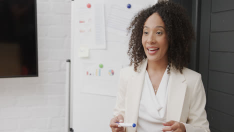 happy biracial businesswoman by whiteboard talking at office meeting, in slow motion