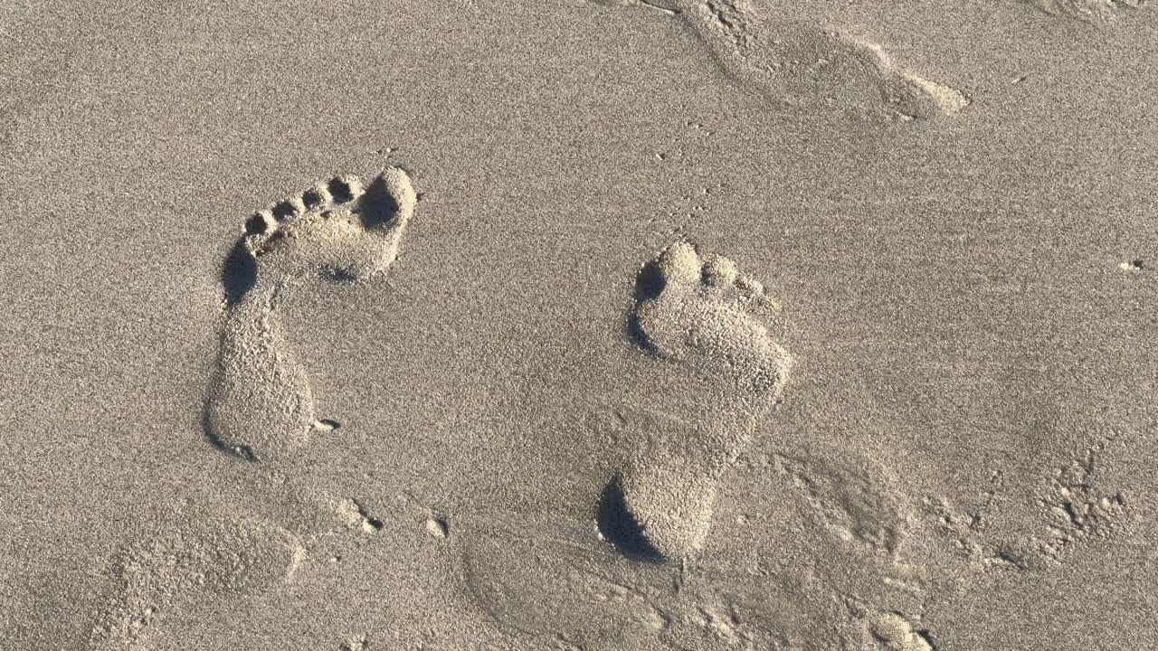 Bir plajda, kıyı şeridindeki kumların üzerinde ayak izleri