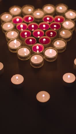 vertical video of romantic red and white candles in the shape of a heart on black background