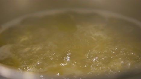 water boiling and bubbling in a stainless pot in the kitchen, steam, vapor, close up shot