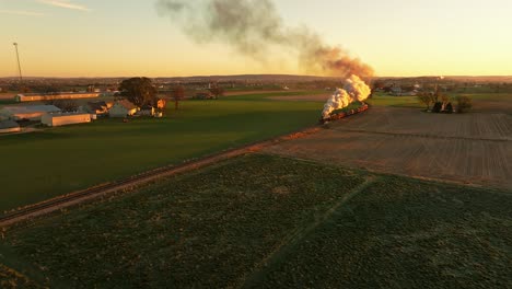 drone view of a steam engine approaching blowing lots of smoke at sunrise traveling thru the farmlands on fall morning