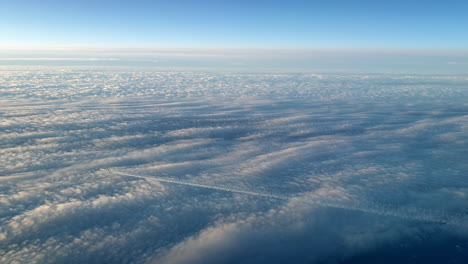 incredible view from the cockpit of an airplane flying high above the clouds leaving a long white condensation vapour air trail in the blue sky