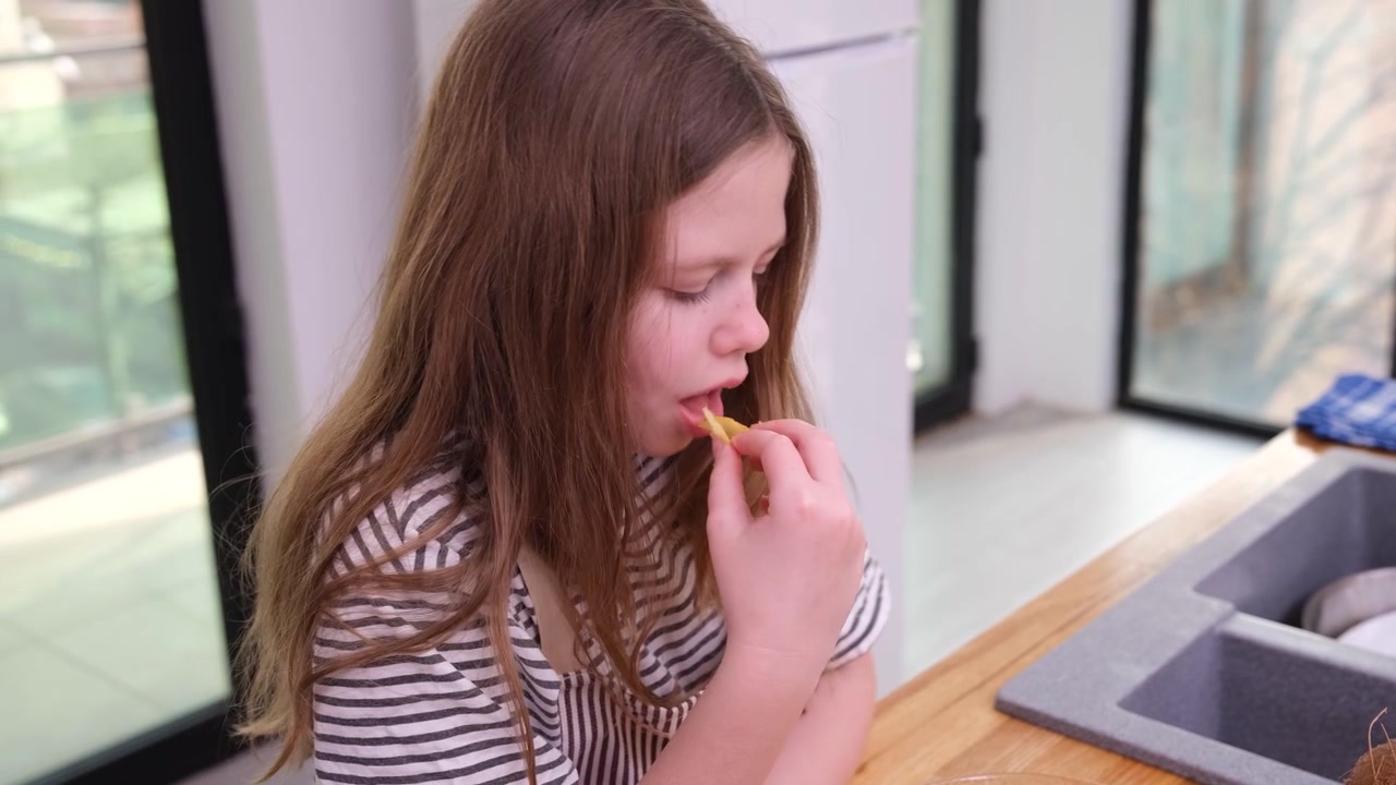 Thoughtful girl tastes food while sitting at kitchen table