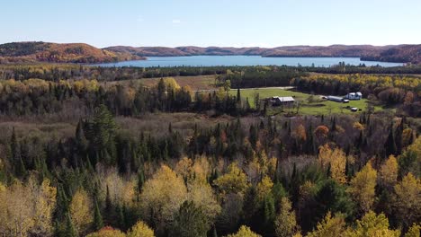 Drone flies an aerial over forest cabin and trees in fall colors.