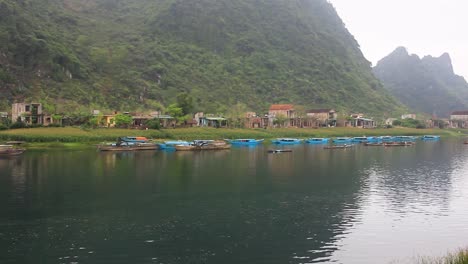 pan del paisaje de la orilla del río en phong nha ke bang, vietnam del norte, por la mañana, con niebla, vista de los barcos y casas tradicionales y un pescador en el trabajo