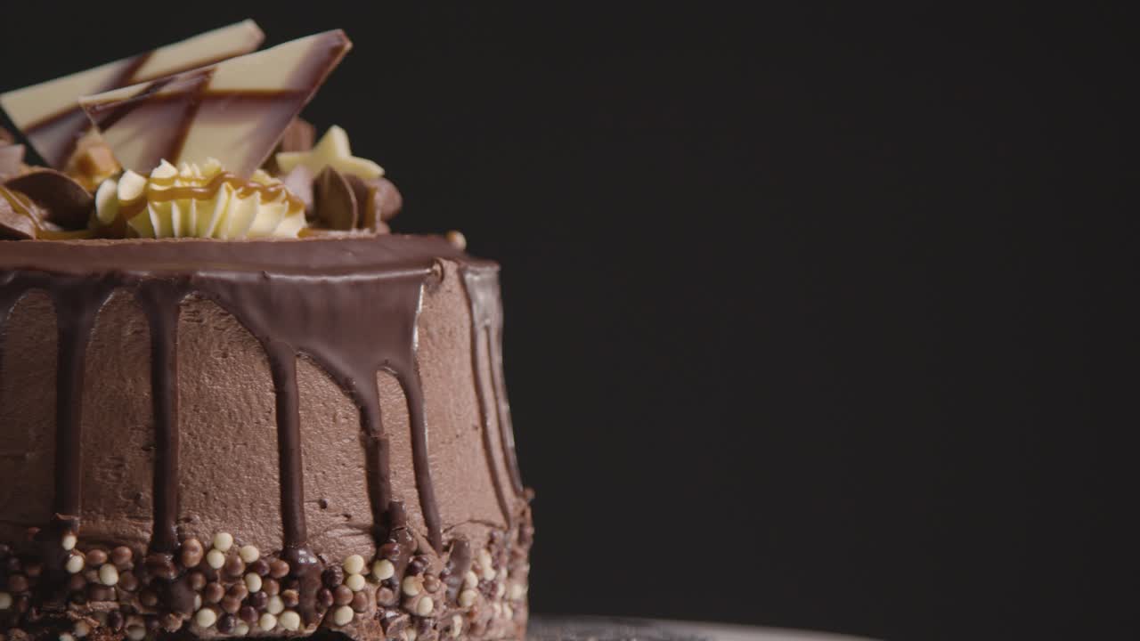 검정색 배경 1에 대해 회전하는 갓 구워지고 장식된 초콜릿 축하 케이크의 스튜디오 샷을 닫습니다.