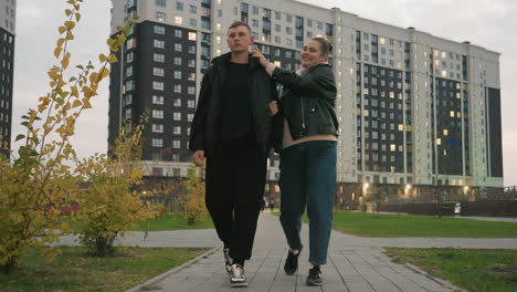romantic moment as couple walk along paved path in urban park while smiling lady playfully tickles her partner who tries to tickle her back but she gently holds his hand teasingly with affection