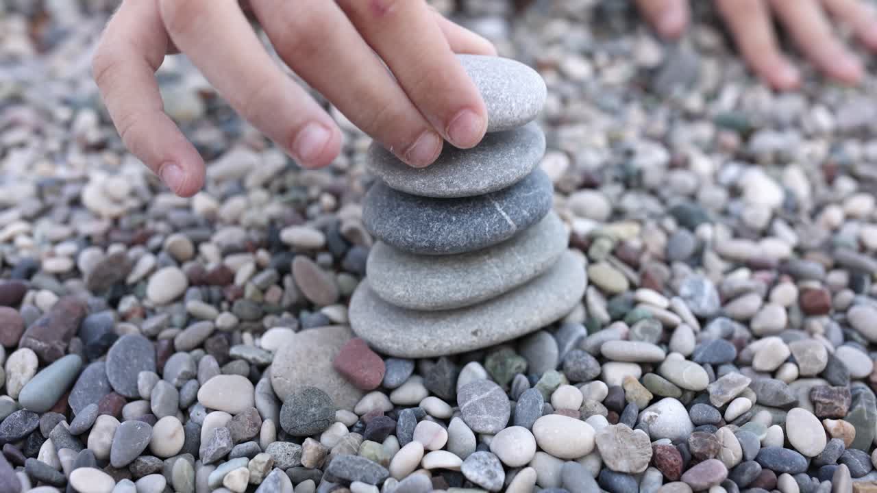 Mani di bambini costruiscono una torre di pietre sulla spiaggia