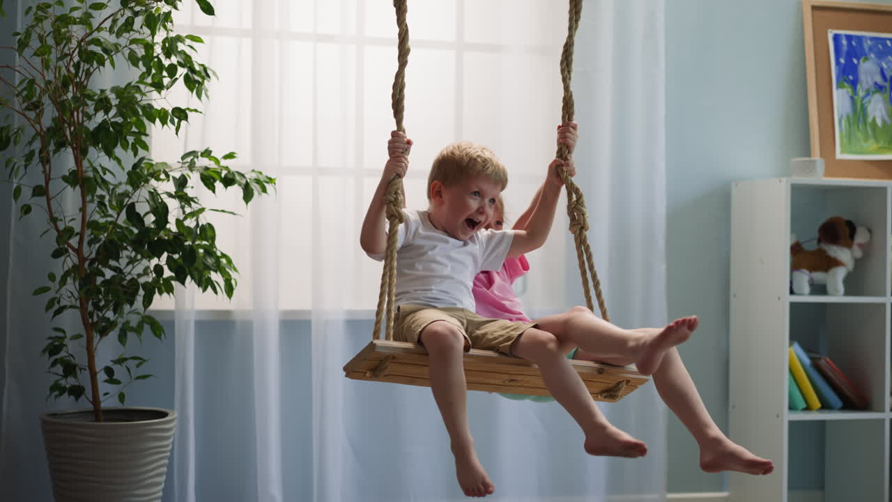 hermano y hermana felices sentados en el columpio cerca de la ventana riendo