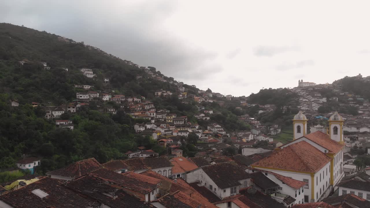 Aerial view of rooftops and Our Lady of Conception church in Ouro Preto, Minas Gerais, Brazil, where Aleijandinho lived with a wider view of the colonial mining valley on an overcast day