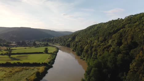 aerial drone footage crossing the river wye with tintern abbey in the background on a sunny summer day, capturing scenic landscapes and historic architecture.