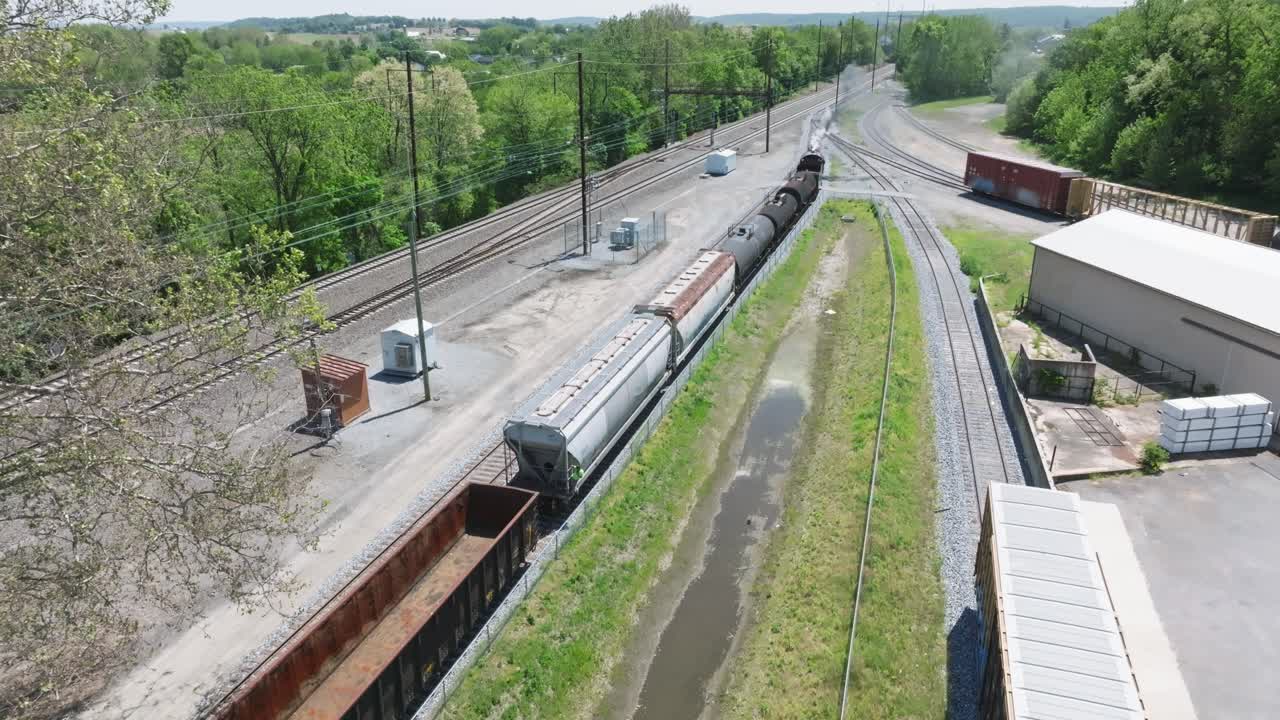A vintage steam freight train makes its way backing up in yard performing switching operations moving steadily along the railway tracks in a peaceful countryside setting