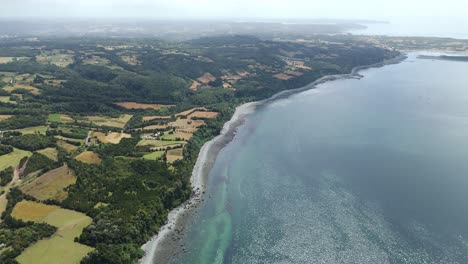 A mesmerizing high-angle view of Lemuy Island's coastline featuring clear waters and lush greenery. push forward, tilt up