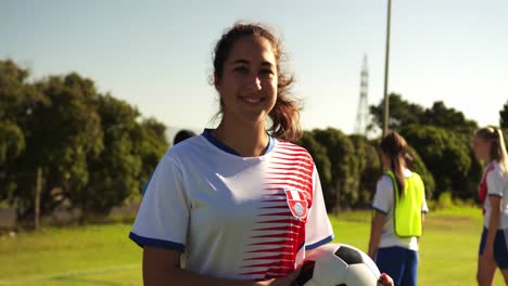 female soccer player holding the ball while teammates train on soccer field. 4k